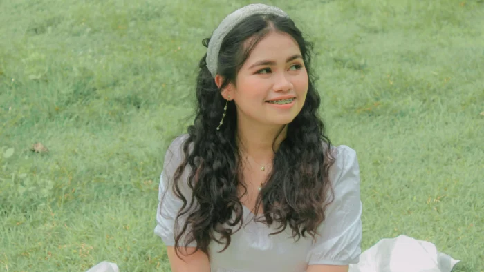 Young woman smiling with braces, sitting on grass, highlighting gummy smile braces cost